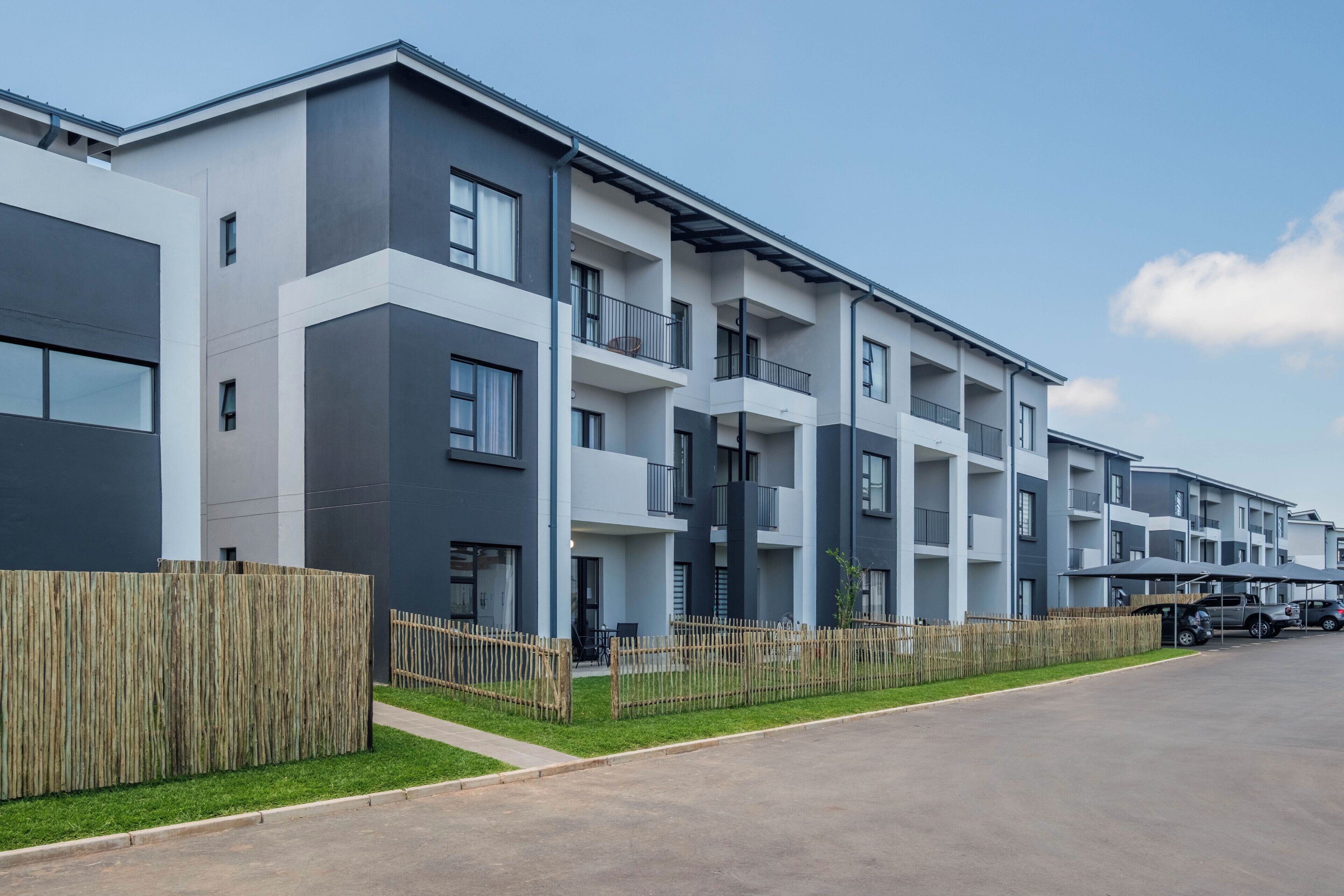 Um edifício residencial moderno de vários andares, com sacadas, cerca de madeira e entrada com calçada.