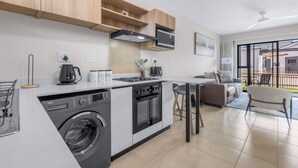 A modern kitchen with a built-in washer, oven, and stove, a dining area with a table and chairs, and a view of the outside through large windows. - Bliss Ballito | Comfort and Style 2x Bedroom (Dolphin Coast)