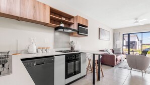 A modern kitchen with integrated appliances, a dining area with a sofa, and a view of the outdoors. - Bliss Ballito | Modern Apartment and Clubhouse (Dolphin Coast)