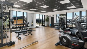 Een sportschool met gewichthefapparatuur, loopbanden en een groot raam met uitzicht op de buitenwereld.