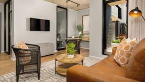Een moderne woonkamer met een bank, twee stoelen, een salontafel en een aan de muur bevestigde televisie.
