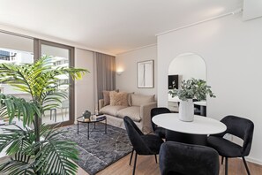 A modern living room with a sofa, a coffee table, and a dining table with chairs. There is a large mirror on the wall and a potted plant on the floor. - Dolce Vita | Designer Sea Point Apartment (Cape Town)