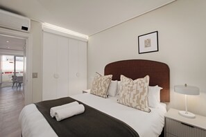 Ein modernes Hotelzimmer mit einem ordentlich bezogenen Bett, einem Nachttisch mit Lampe und einem gerahmten Bild an der Wand.
