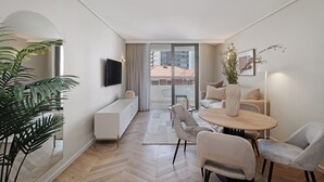 Un soggiorno moderno con divano, tavolo da pranzo e sedie. C’è una TV a parete e una pianta sul pavimento.
