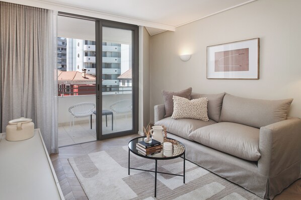 Ein modernes Wohnzimmer mit einer Couch, einem Couchtisch und Blick auf einen Balkon mit Stühlen.