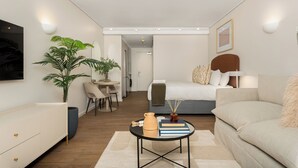 A modern, well-lit hotel room with a bed, sofa, dining area, and a large potted plant. - Dolce Vita | Designer Apartment | Lion's Head View (Cape Town)