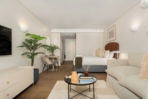 A modern, well-lit hotel room with a bed, sofa, dining area, and a large potted plant. - Dolce Vita | Designer Apartment | Lion's Head View (Cape Town)