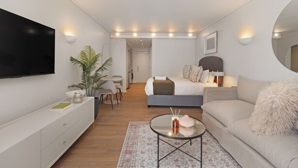 Ein modernes, helles Schlafzimmer mit einem Bett, Nachttisch und einem an der Wand montierten Fernseher.