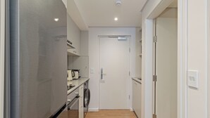 Ein schmaler Flur mit einem Edelstahlkühlschrank, einer Mikrowelle und einer kleinen Küchenzeile.