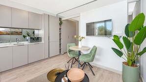A modern kitchen with grey cabinets, a white countertop, and a built-in microwave. There is a round table with two green chairs and a potted plant. - One Rosebank Premium Luxe Apartment (Johannesburg)