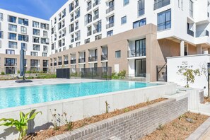 Un edificio moderno con piscina, varios balcones y entrada protegida.
