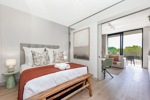 Un dormitorio moderno con una cama grande, un banco, un escritorio y vistas al exterior.