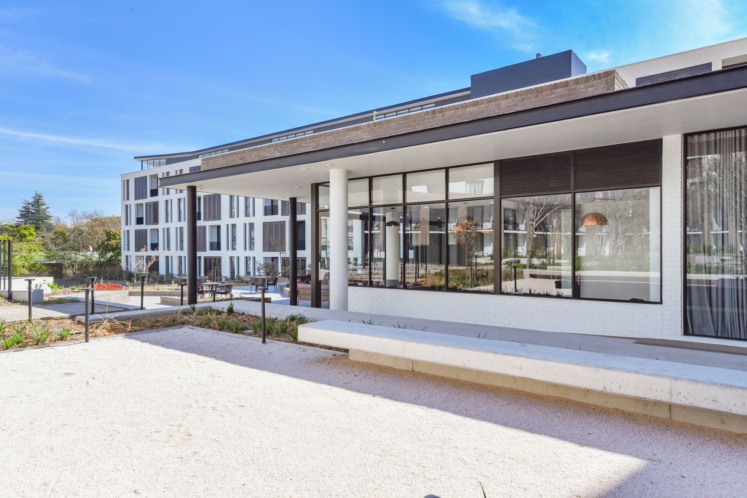 Un edificio moderno con amplios ventanales, techo plano y zona pavimentada con mesas al aire libre.