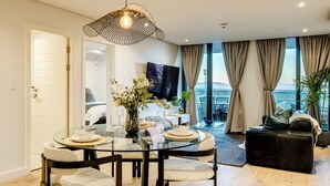 Ein modernes Wohnzimmer mit einem Glastisch, einer schwarzen Ledersofa und einem großen Fenster mit Vorhängen.