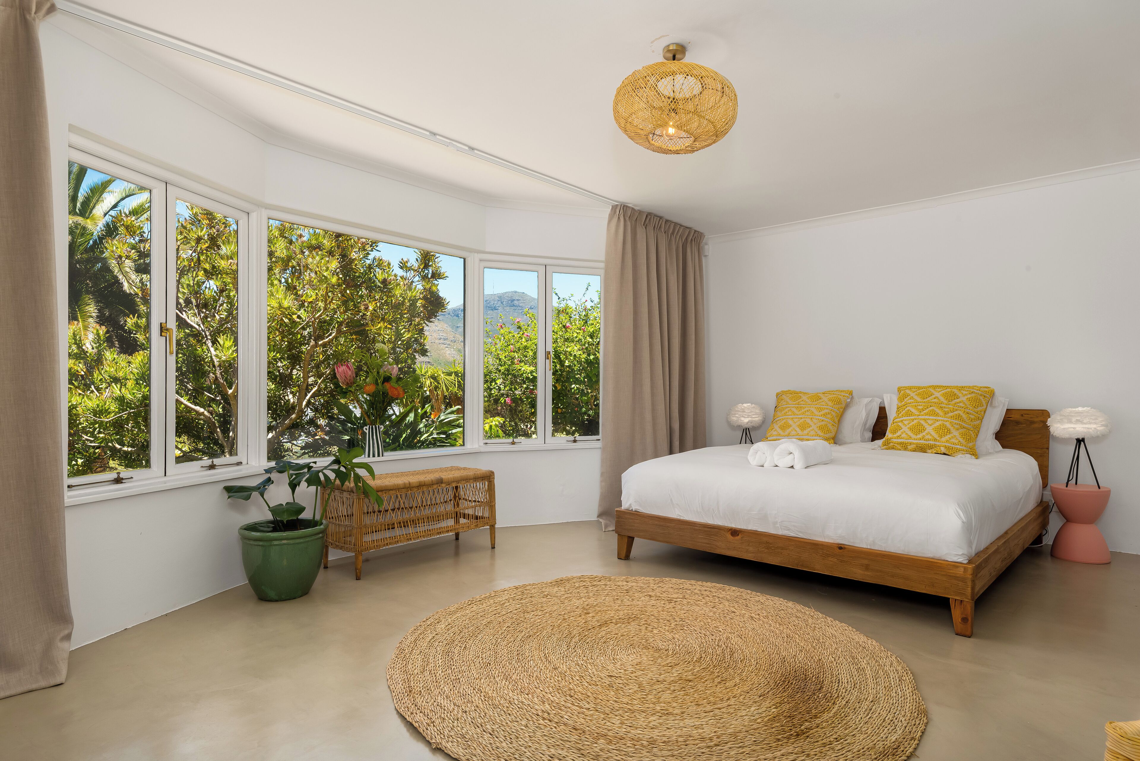 A bedroom with a large bed, a view of greenery outside, and a wicker floor mat.