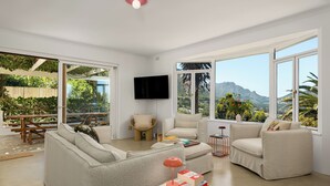 A spacious living room with large windows, a flat-screen TV, and a comfortable seating area. - 5BD Villa with Mountain Views, Pool and Braai (Cape Town)