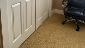 A room with a beige carpet, a black office chair, and white double doors.
