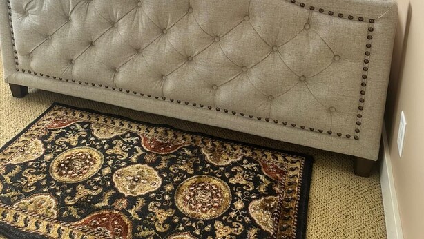 A bedroom with a tufted headboard, a patterned bedspread, and a decorative rug.