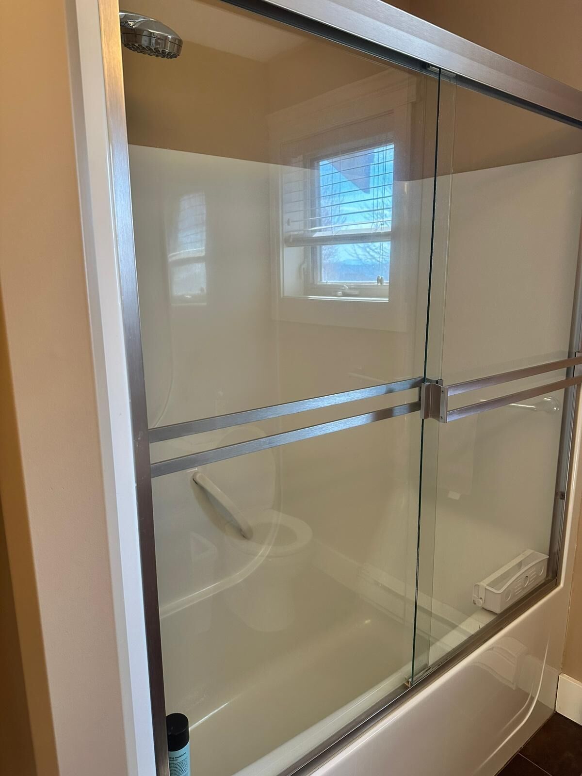 A glass-enclosed shower with a window, a white bathtub, and a visible shower control panel.