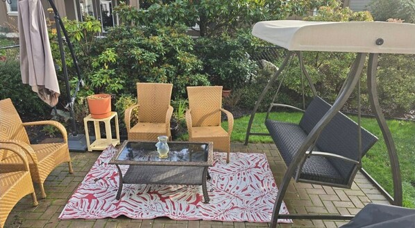 An outdoor patio area with wicker chairs, a glass table, and a swing chair. - Comfortable GuestRoom in Quiet Echo Valley (Victoria)
