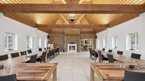 Un vaste espace dédié à la salle à manger, avec une longue table en bois, des chaises noires et une cheminée en pierre.