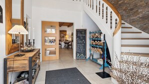 Un escalier avec une main courante en bois et une balustrade blanche, menant à une pièce dotée d’une porte en bois et d’un tableau noir servant de menu.