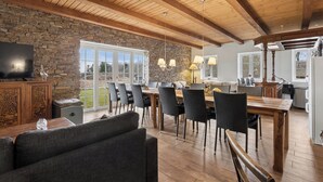 Une salle à manger spacieuse avec un mur en pierre, des poutres en bois au plafond et une grande fenêtre.