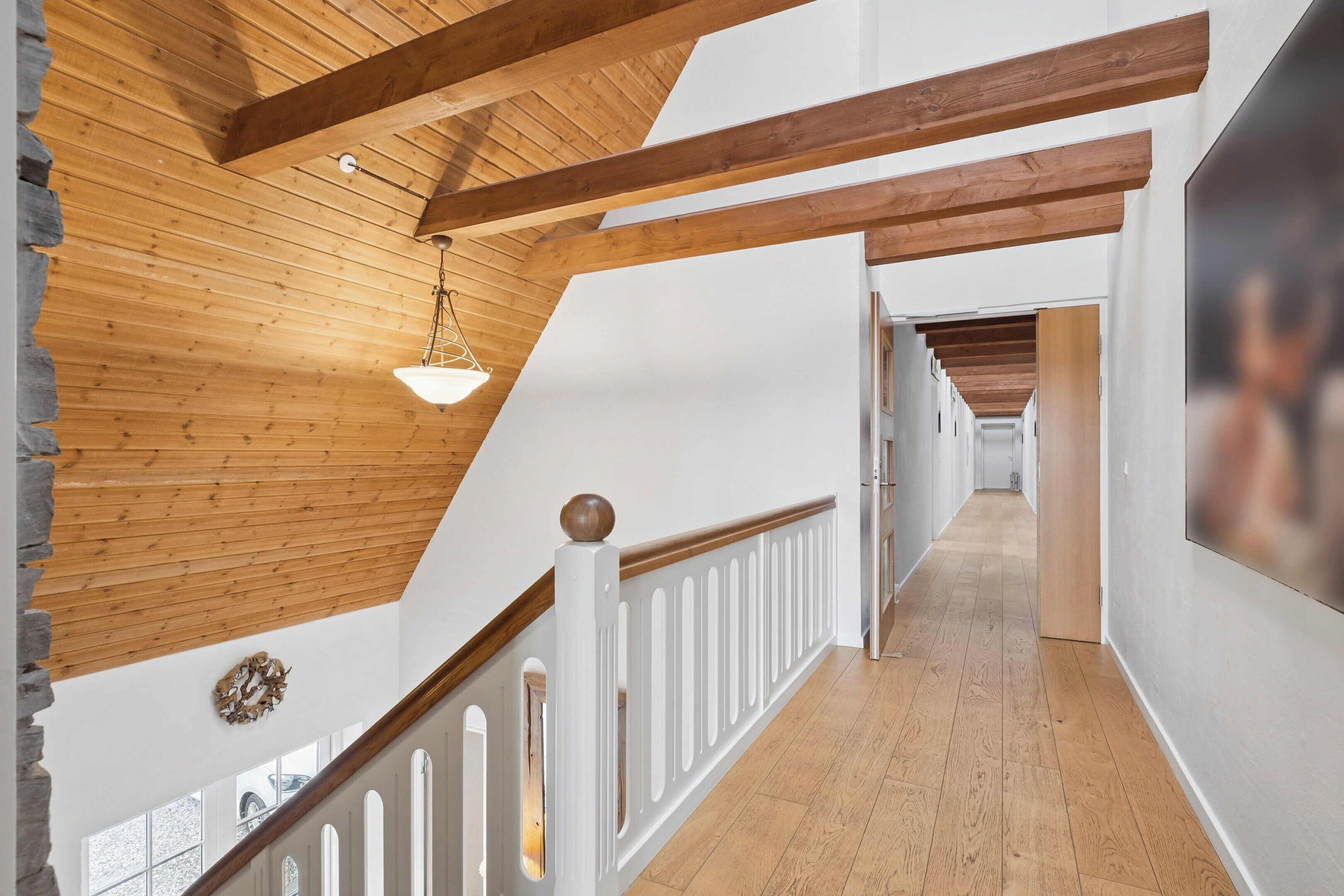 Un plafond en bois avec des poutres apparentes, une rambarde blanche et un couloir menant à une autre pièce.