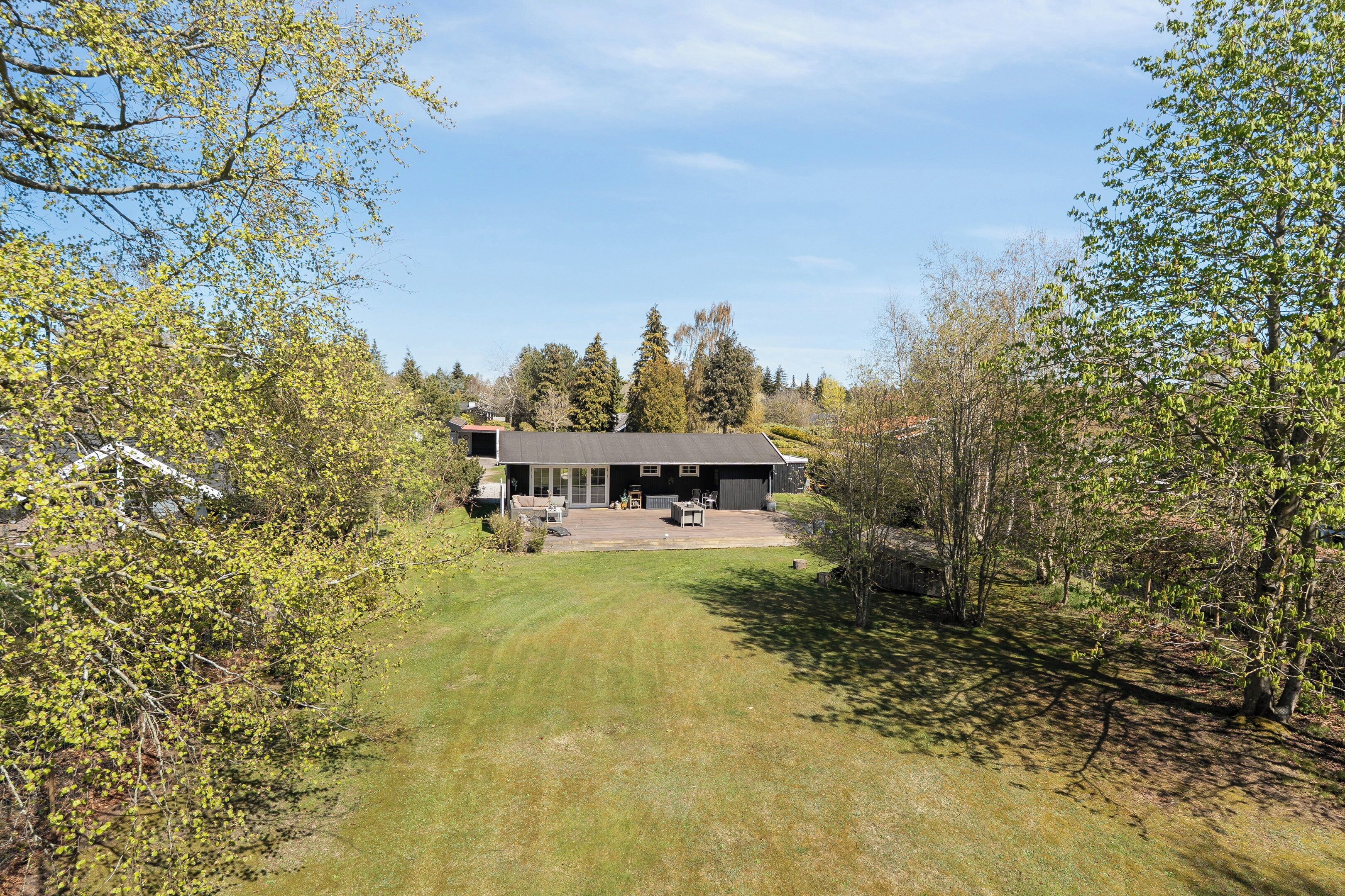 Een modern huis met een ruim terras, omgeven door bomen en een verzorgd gazon.