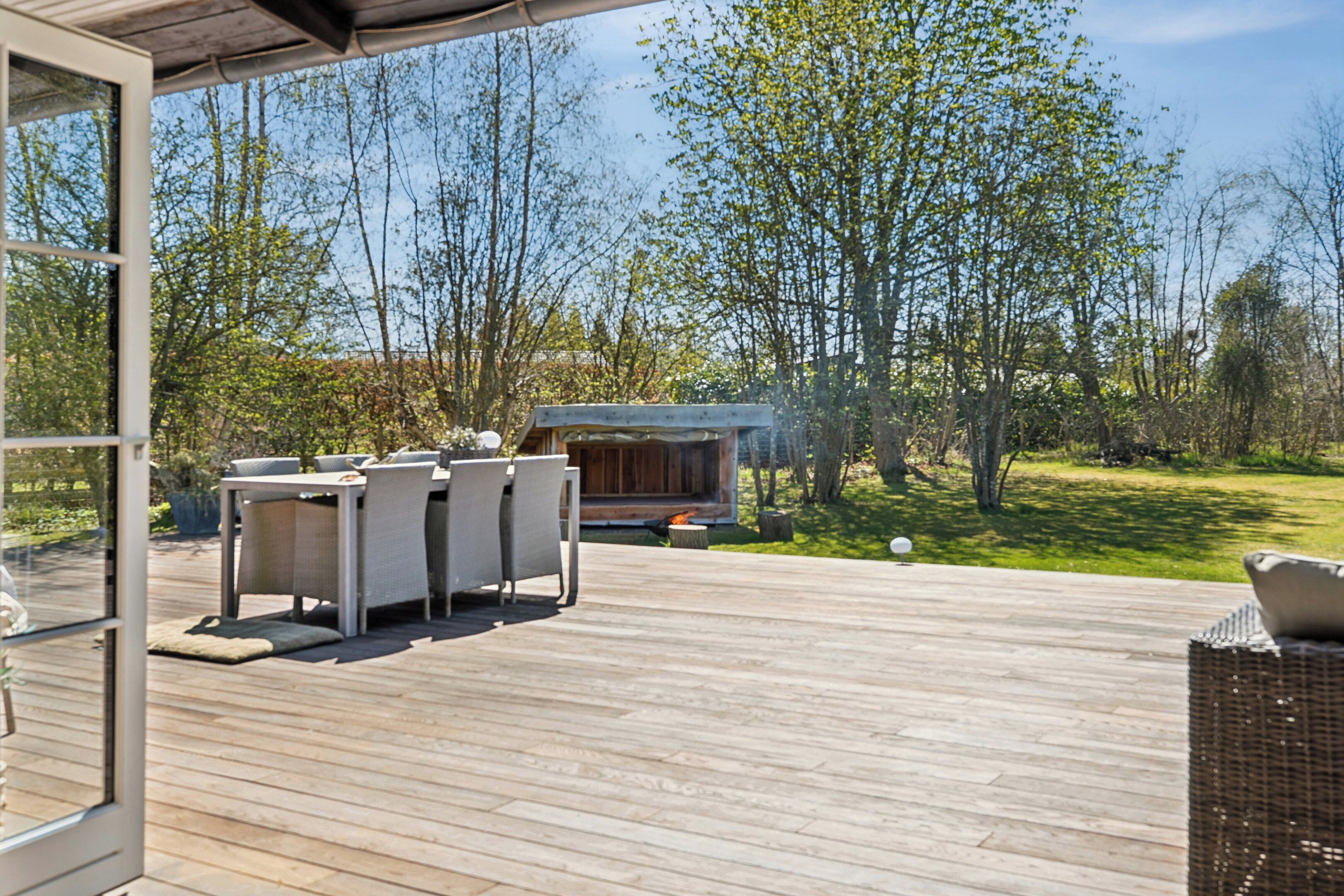 Een houten terras buiten met een eethoek en een jacuzzi.