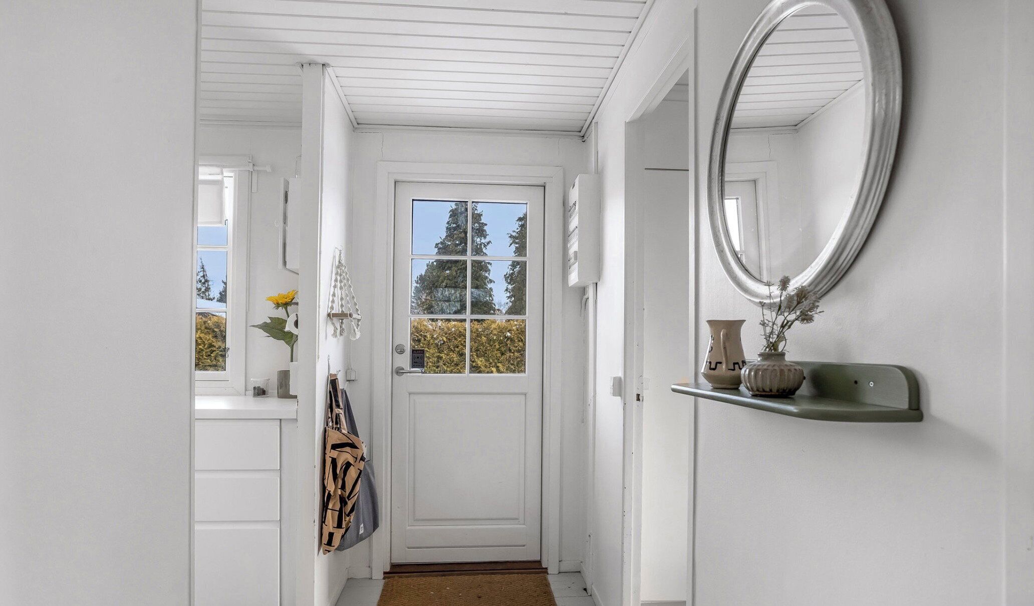 A white hallway with a door, a mirror, and a shelf with a vase.