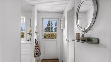 A white hallway with a door, a mirror, and a shelf with a vase.
