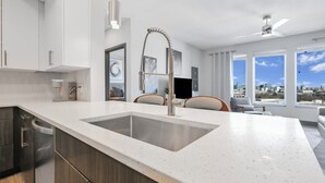 A modern kitchen with a large island, stainless steel appliances, and a city view through large windows. - Nashville KING BED, Gym, Rooftop Pool, Parking (Nashville)