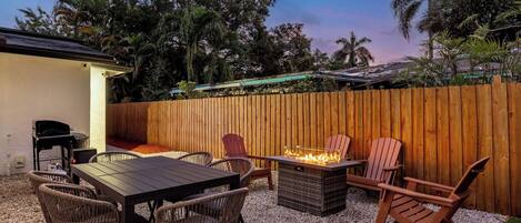 A patio with a table and chairs, a fire pit, and a wooden fence.