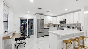 A modern kitchen with white cabinets, stainless steel appliances, and a bar area with stools.