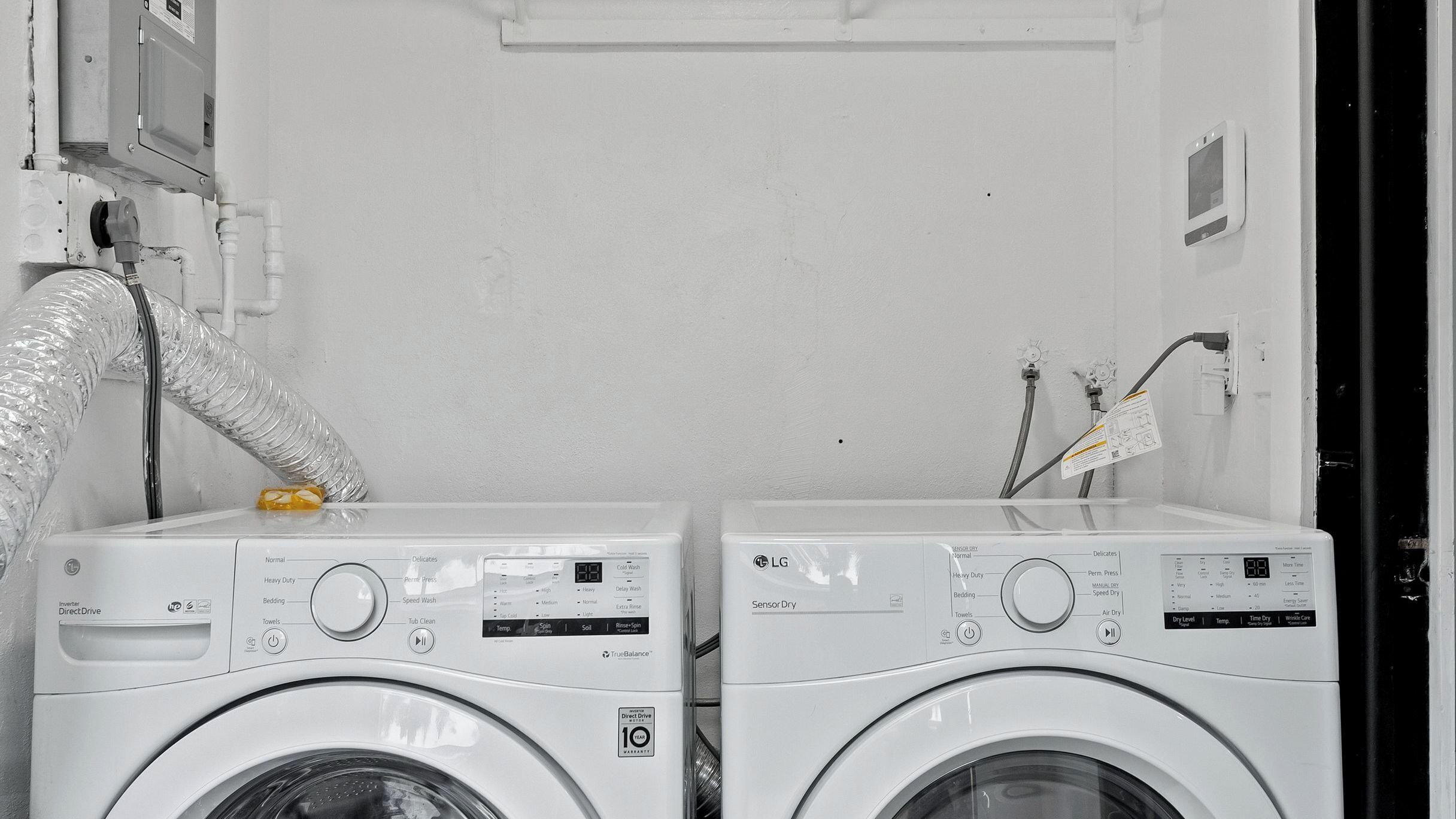 Two white washing machines with control panels, a vent hose, and a power outlet on the wall.