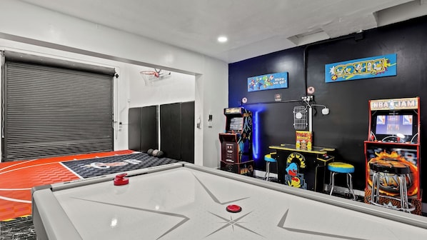 A recreational room with a shuffleboard table, arcade games, and a basketball hoop.