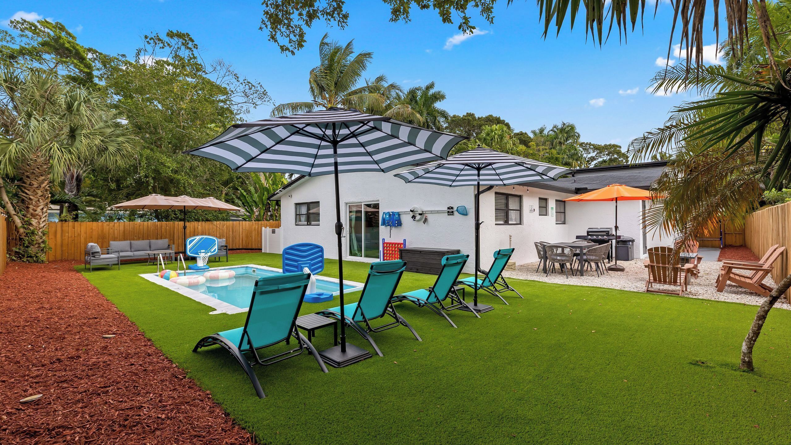A backyard with a pool, lounge chairs, a barbecue area, and a small house.