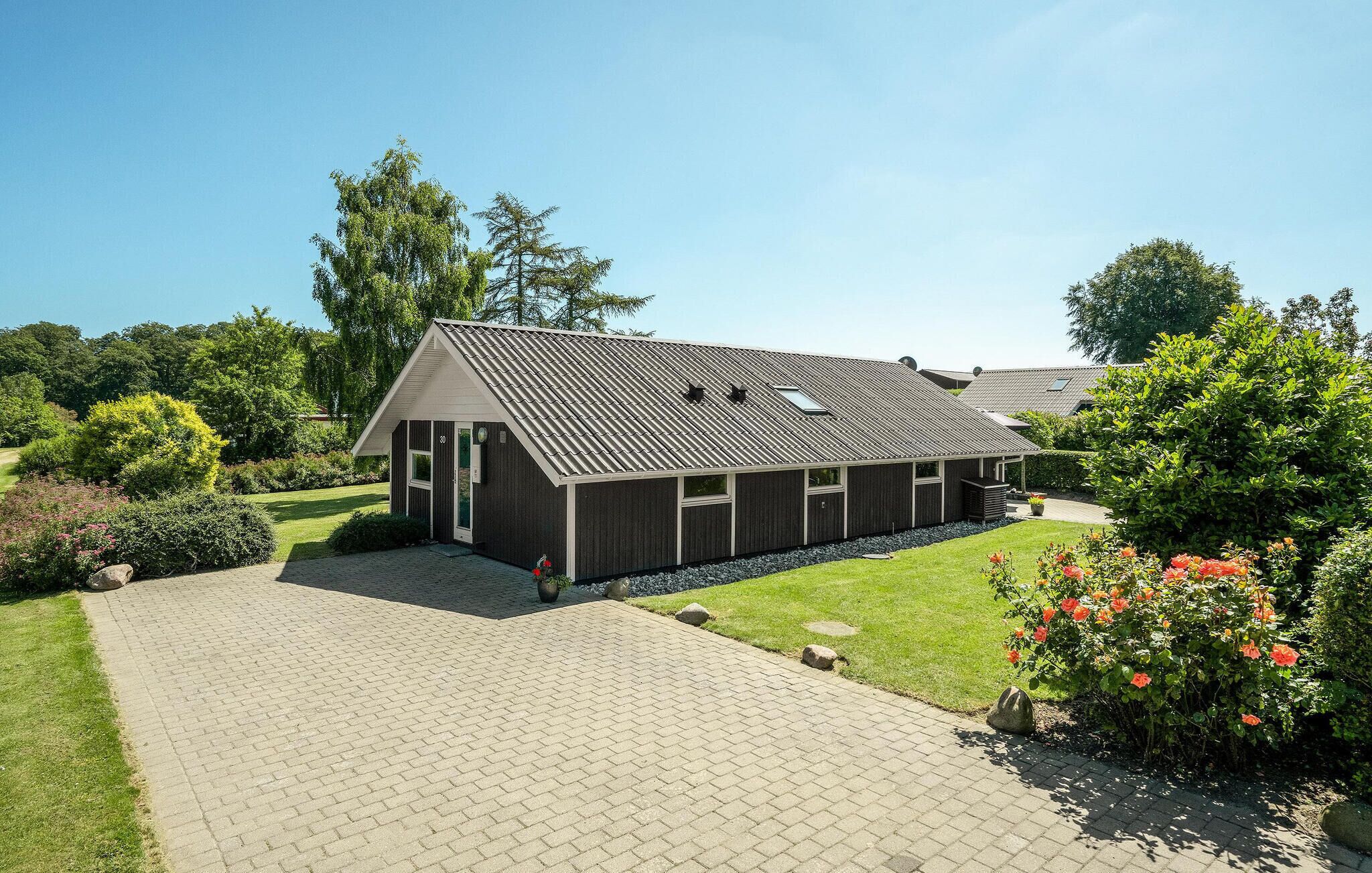 Een modern huis met een schuin dak, een verharde oprit en een verzorgde tuin met bloemen en struiken.
