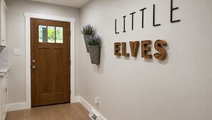 Ein Flur mit einer Holztür, einem an der Wand befestigten Schild mit der Aufschrift 'LITTLE ELVES' und einer hängenden Pflanze.