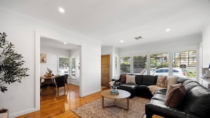 Uma sala de estar moderna com um sofá de couro preto, uma mesa de centro e uma área de jantar com mesa e cadeiras de madeira.