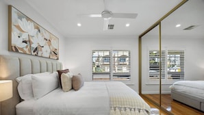 Quarto moderno com uma cama grande, ventilador de teto e janelas amplas com persianas.