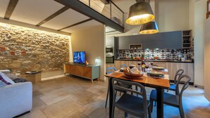 A modern kitchen with a stone wall, wooden ceiling beams, and a dining area with a table set for four. - San Gaggio - Two Bedroom Apartment, Sleeps 5 (Florence)