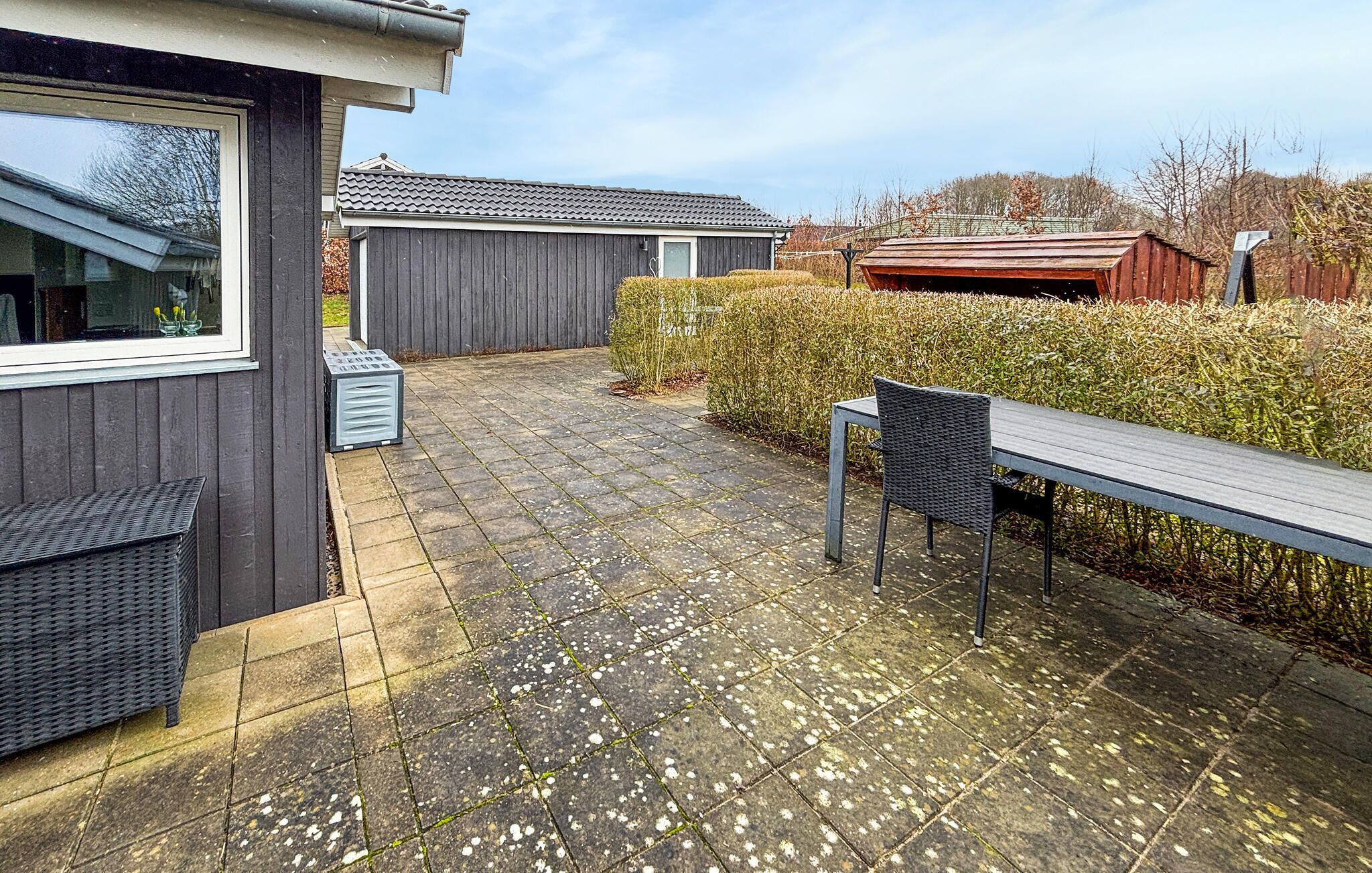 Eine Terrasse mit Tisch und Stühlen, eine kleine Gartenhütte und ein Holzzaun.