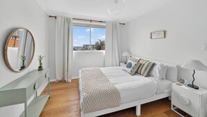 A bedroom with a bed, bedside table, lamp, and a window with curtains. - Coogee Oasis Ocean Outlooks near the Beach (Coogee)
