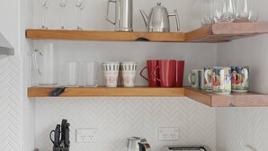 A kitchen with three wooden shelves holding various kitchenware, including glassware, cups, and a toaster. - Coogee Oasis Ocean Outlooks near the Beach (Coogee)
