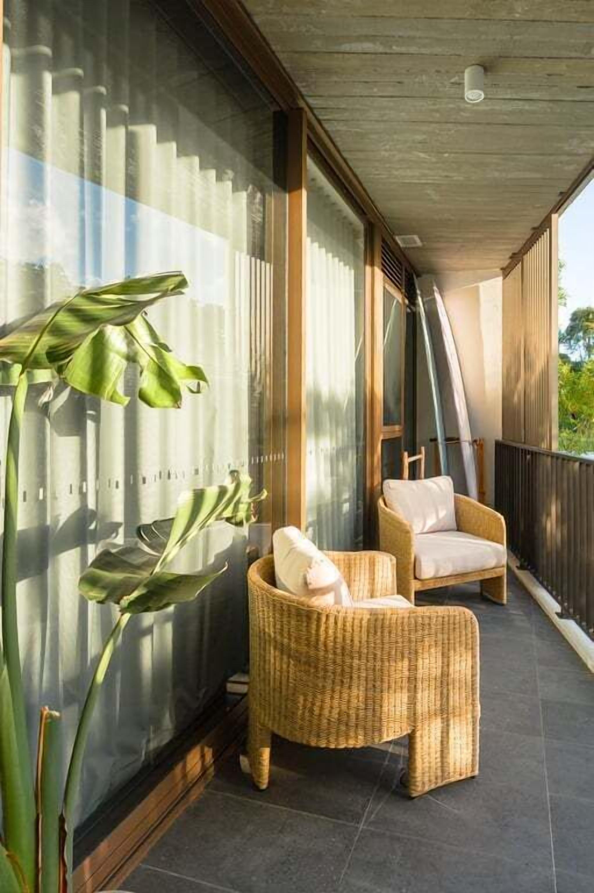 Un balcon avec des fauteuils en osier, une grande plante et une vue sur l’extérieur.