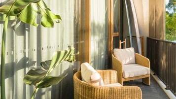 Un balcon avec des fauteuils en osier, une grande plante et une vue sur l’extérieur.