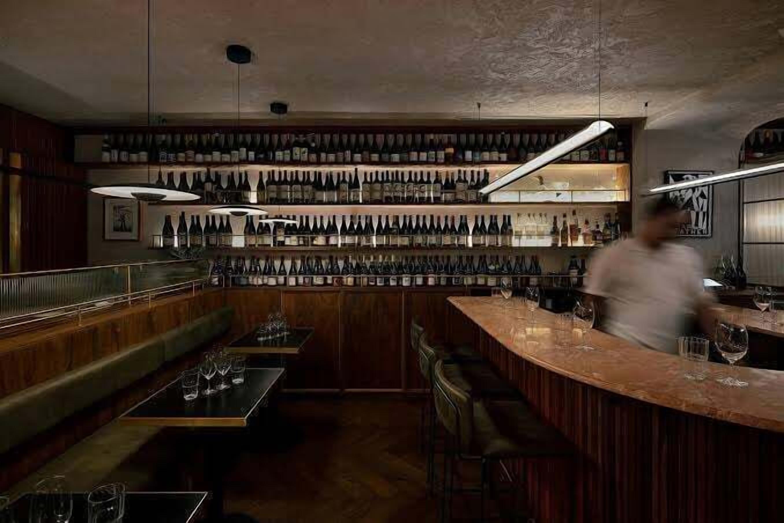 A bar area with a long counter, multiple seating options, and a wine rack in the background.