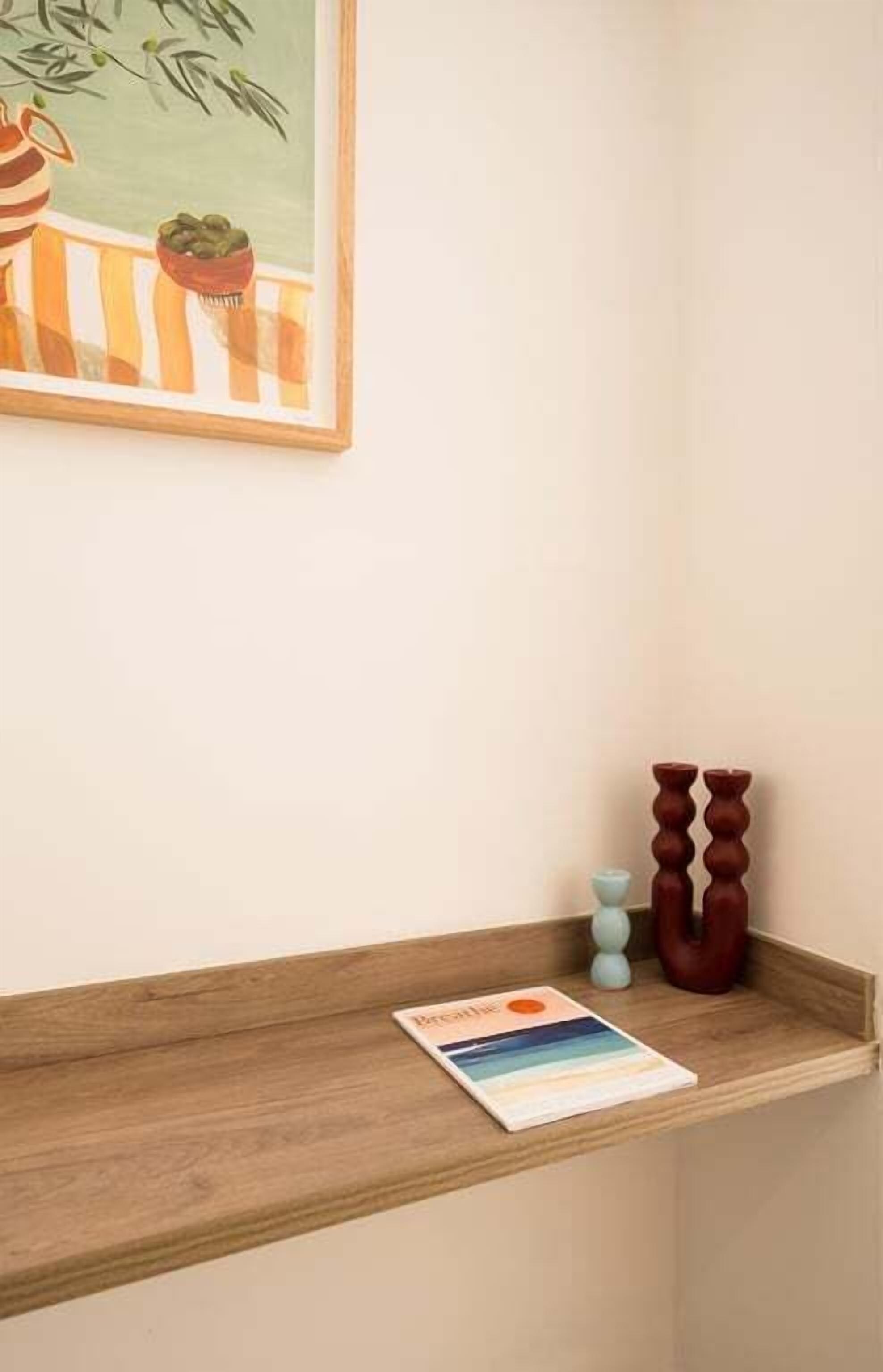 Una estantería de madera con un cuadro enmarco, una planta pequeña en maceta y un candelabro.